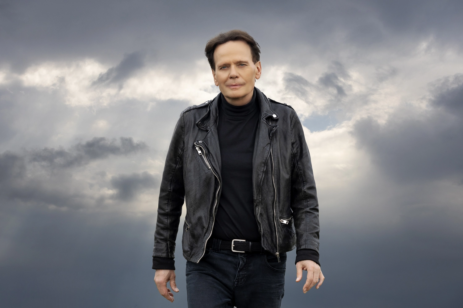CF Christian Franke - Musiker - Christian Franke trägt eine schwarze Lederjacke und einen schwarzen Rollkragenpullover und steht vor einem bewölkten Himmel.